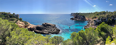 wide shot of a jagged rock cliff coast line meeting a rich turquoise ocean